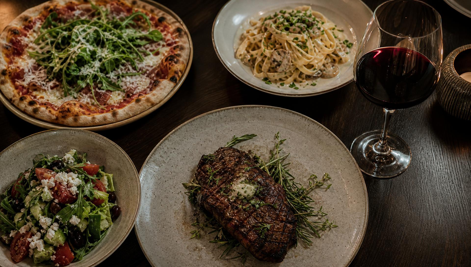 À la carte-rätter serverade på Restaurang Hörnan — biff, pasta, sallad och pizza på ett mörkt träbord